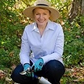 Michele MacKinnon kneeling in garden with gardening shovel