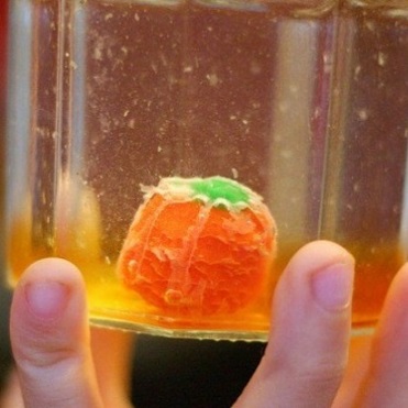 child's hand holding a beaker with candy pumpkin inside