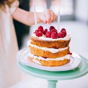 strawberry shortcake on a cake plate with child placing candles in it