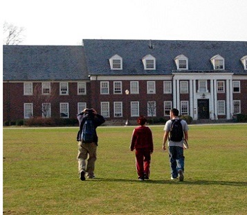 three students with backpacks walking across the lawn heading towards college building