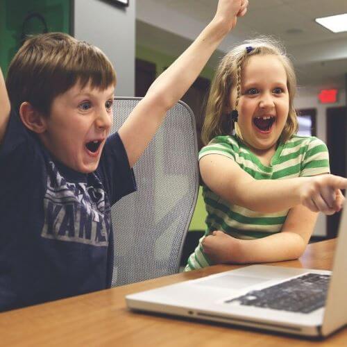 Boy and Girl sitting at computer and excitedly pointing at it