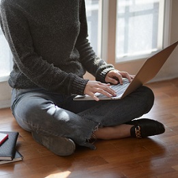 person sitting cross legged on floor, typing on laptop computer on their lap
