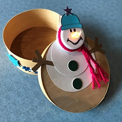 small round box topped with cardstock snowman with pink yarn scarf, blue hat and tealight for head