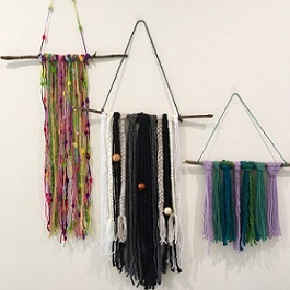 colorful braided yarn looped over a stick with yarn attached to hang artwork with