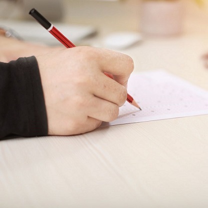 hand holding red pencil filling out bubbles on test answer sheet