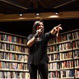 woman on stage holding microphone and pointing out into audience