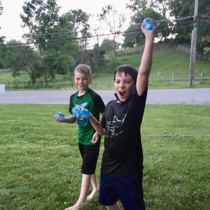 two soaking wets boys holding up water balloons in victory