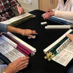 four people playing mahjong, game pieces and hands seen only