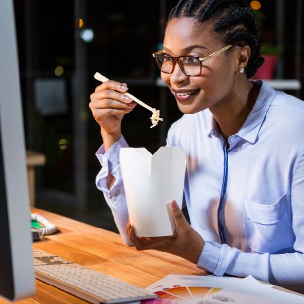 woman at desk eating chinese food while looking at computer screen