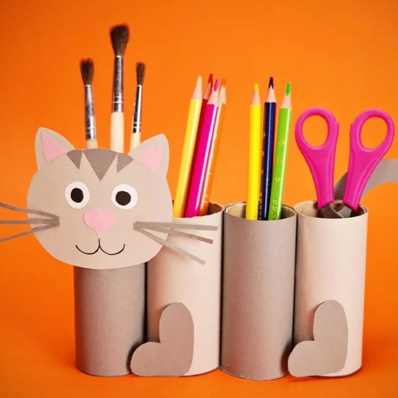 four toilet paper rolls glues together and decorated with a cat face and tail to make a feline pencil and scissor holder