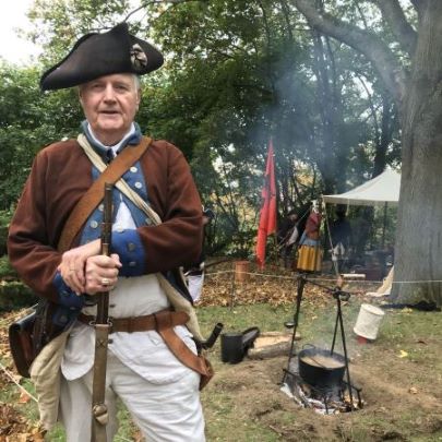 man dressed in Revolutionary War clothing, leaning on a musket