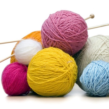 pile of colorful balls of yarn with knitting needles stuck through them
