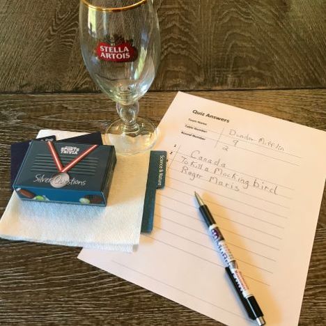 table top with trivia answer sheet, pen, empty beer glass and trivia card on top