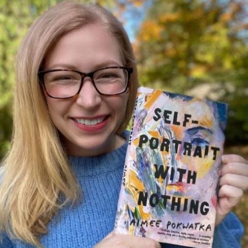 Blond womanwith blue sweater and glasses holding up a book titled Self-Portrait with Nothing"