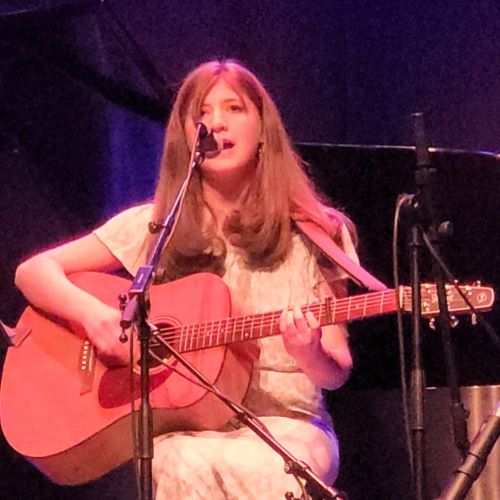 girl playing a guitar and singing into a microphone
