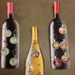 three cardstock wine bottles with homemade wine charms on them