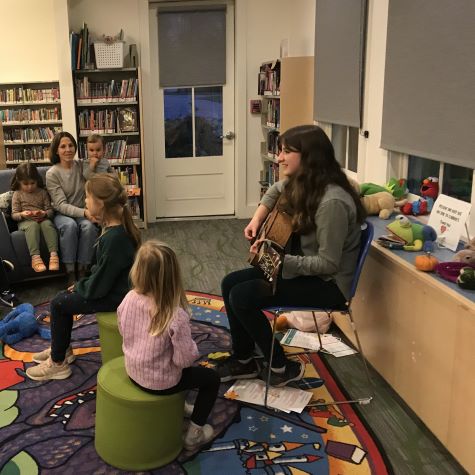 Teen girl playing guitar and singing to room full of preschool children