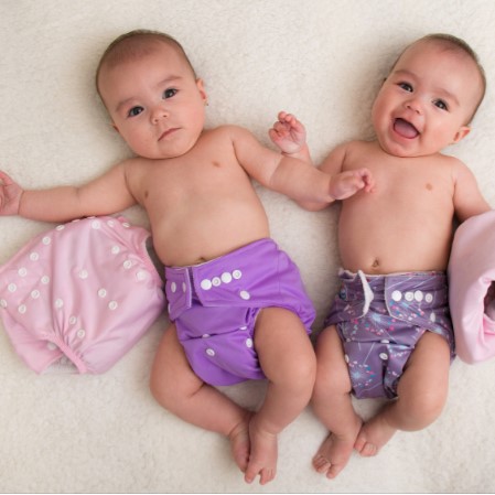 Twin babies laying on white rug and wearing colorful purple cloth diapers