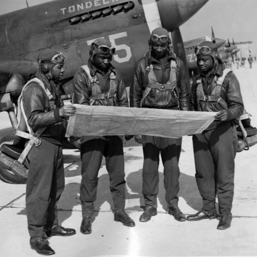 Four African American male pilots looking at a map alongside their plane