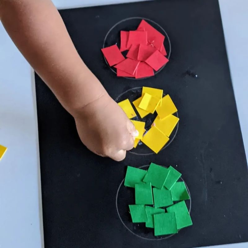 black construction paper with 3 vertical circles filled with red, yellow and green bits of paper