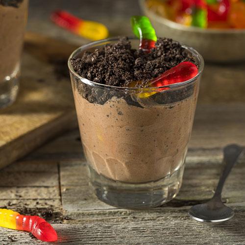 chocolate pudding in clear cup with layer of crumbled cookies and gummy worms on top