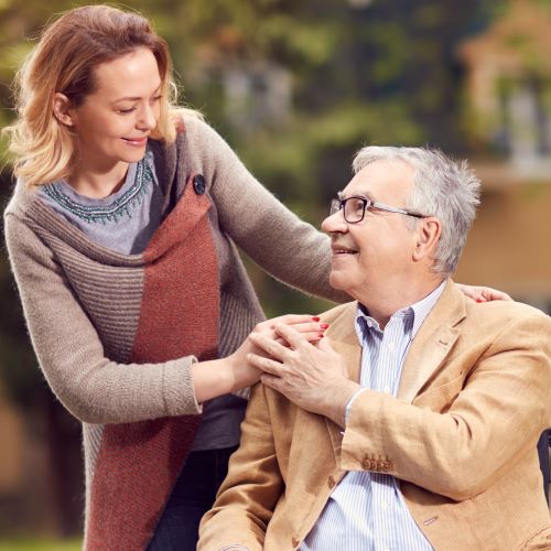 older couple with woman standing with hand on shoulder of seated man