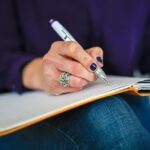 person writing in notebook balanced on their lap