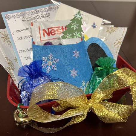 basket decorated with bells and ribbons, and containing a felt mug with cocoa packet and treats