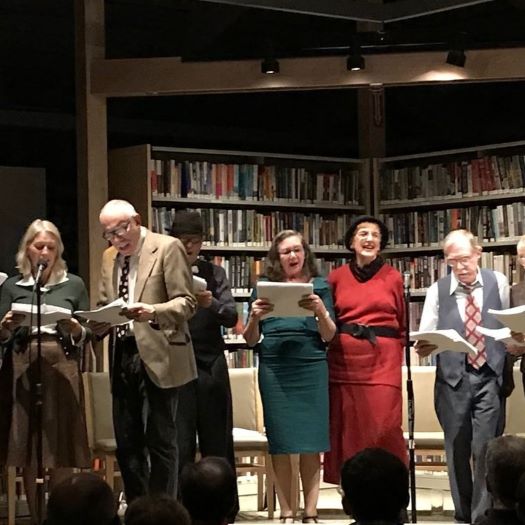 Adults dressed in vintage clothing reading from scripts on a stage