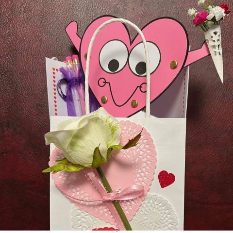 paper bag decorated with lace hearts and a silk rose, with a valentine peeking out of the top