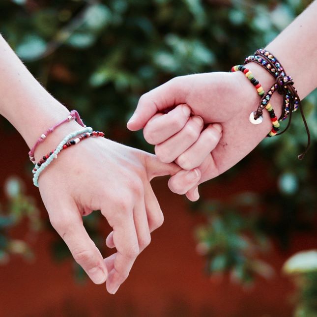 two interlocked hands, both wearing beaded bracelets
