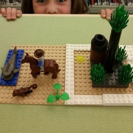 child peering over the table top with a cowboy cactus Lego scene on it