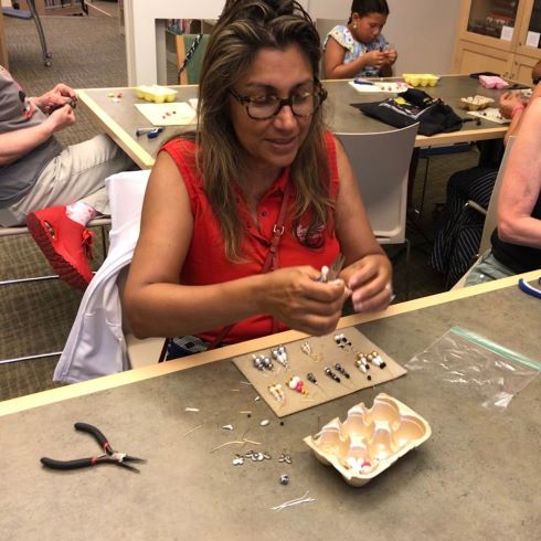 woman putting together pierced earrings with finished pairs and pliers before her