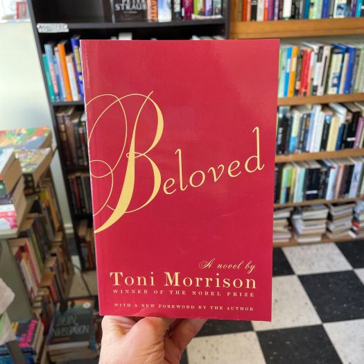 A hand holding up a book with the title "Beloved"