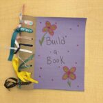 construction paper book bound together with colorful ribbons, with the book title "Build-a-Book"