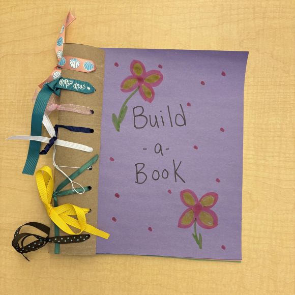 construction paper book bound together with colorful ribbons, with the book title "Build-a-Book"