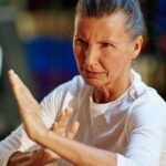 Older woman with gray hair pulled back in bun, with her hands up in self defense gesture