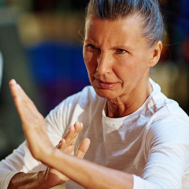 Older woman with gray hair pulled back in bun, with her hands up in self defense gesture