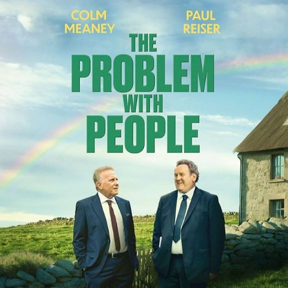 Two older males in suits, standing outside a stone cottage with the movie title The Problem with People overhead
