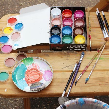 open paint jars in a box, alongside a mixing palette and assorted paintbrushes