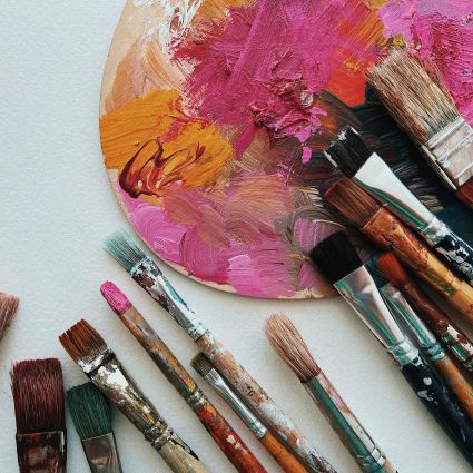 messy paint palette surrounded by assorted size paintbrushes.