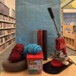 Table topped with craft items: yarn, play dough, button maker and shiny paper