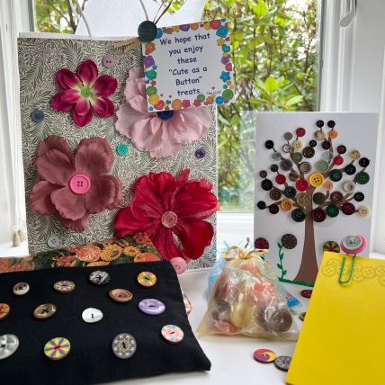 A gift bag decorated with flowers made of buttons, next to a black pillow with colorful buttons displayed on it, and a greeting card decorated with a tree made of buttons