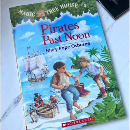 Book titled Pirates Past Noon above drawing of boy and girl on beach with pirates and ship in the distance