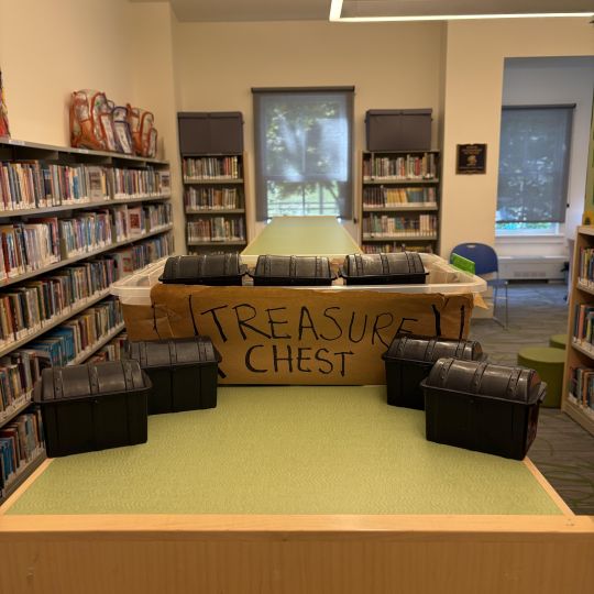 Small plastic treasure chests arranged on a table in front of sign that says Treasure Chest