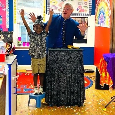 Little boy standing with arms outstretched next to a magician