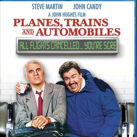 Man in suit and a man in a bulk overcoat seated together on an airport bench