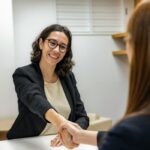 Woman with dark hair and glasses shakng the hand of an interviewer