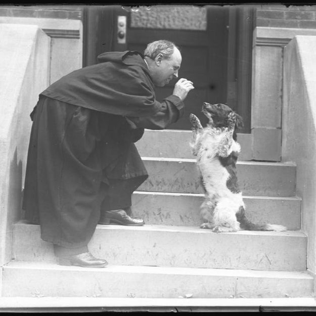 outside steps with priest in robes getting dog to sit up and beg for a treat