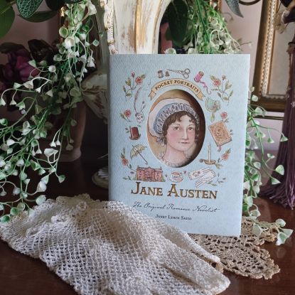a book titled" Jane Austen:The Original Romance Novelist" leaning against a vase of flowers with a lace glove beneath it.